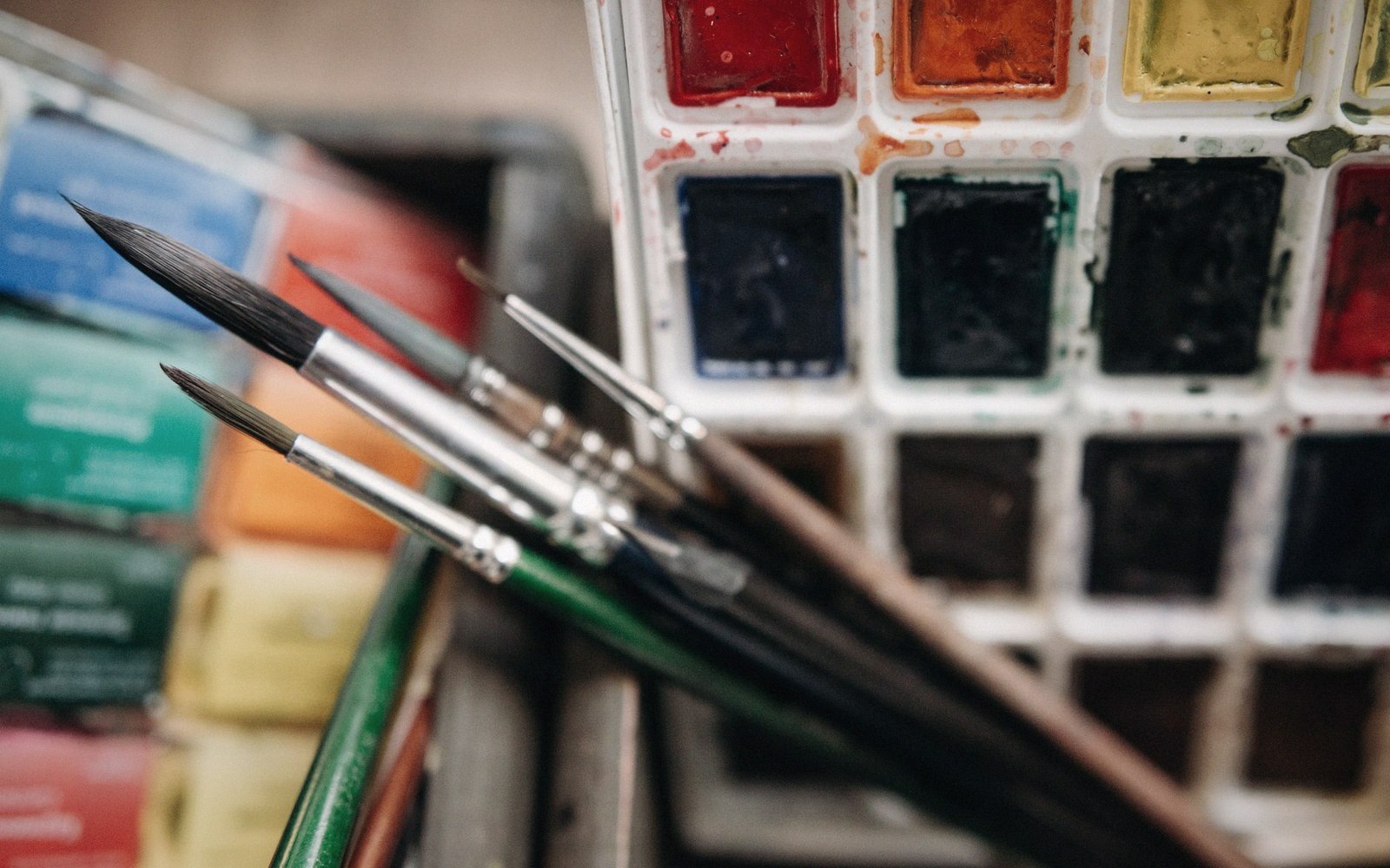 A worn watercolour pan set, pigment dished out, brushes laid across it